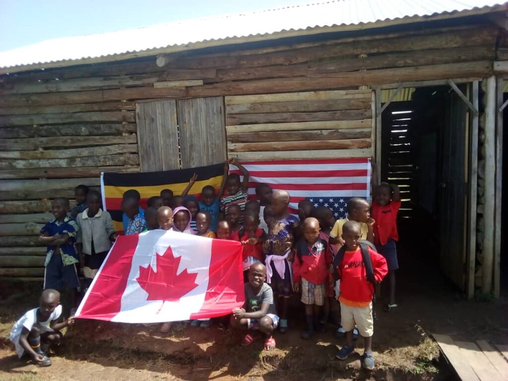 School children holding Canadian flag in front of temporary building for YAVINS Education Centre Uganda